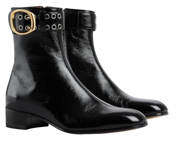 Pair of black leather boots with gold buckles on a light gray background