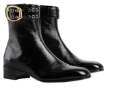 Pair of black leather boots with gold buckles on a light gray background