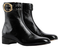 Pair of black leather boots with gold buckles on a light gray background