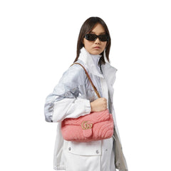 Person holding a pink quilted handbag with a brand logo against a plain background