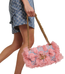 Pink handbag with gold chain and Gucci logo held by a person wearing a blue patterned outfit.