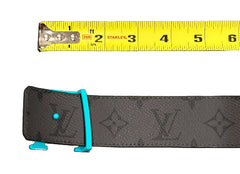 Gray belt with blue buckle being measured by a yellow Stanley tape measure on a gray surface.