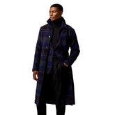 Man wearing a long plaid coat in a white room