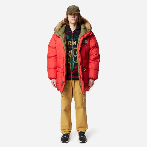 Person wearing a red puffer jacket, patterned sweater, and yellow pants on a white background