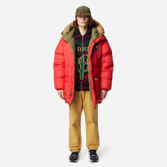Person wearing a red puffer jacket, patterned sweater, and yellow pants on a white background