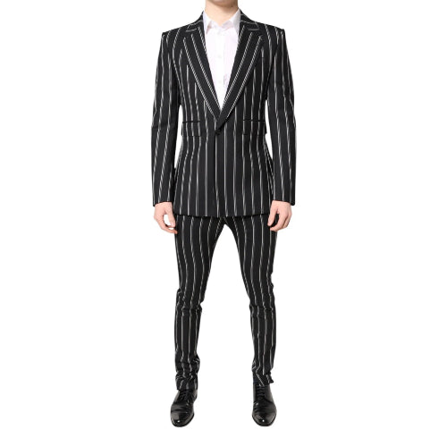A male model wearing a black striped Dolce & Gabbana two-piece pant suit with a white shirt and black shoes.