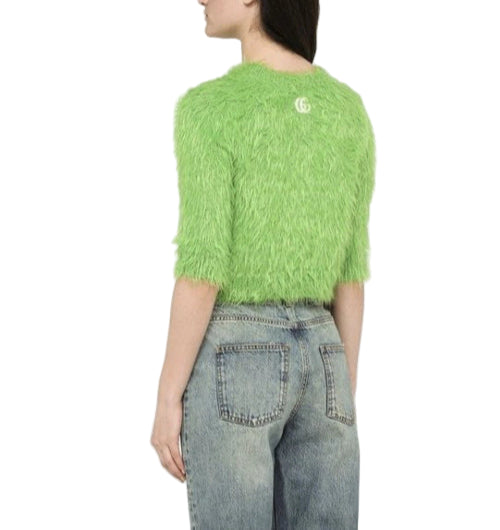 A woman is shown from the back wearing a bright green, fluffy, Gucci crewneck top with 3/4 sleeves and the brand's logo visible on the back neckline.