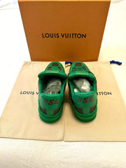 Green children's shoes with red accents on a Louis Vuitton dust bag and box.