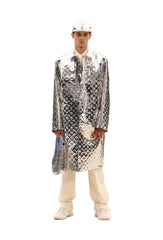 Person wearing a reflective silver jacket with a pattern against a marble wall.