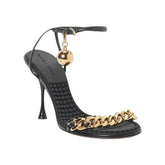 Black high-heeled shoe with gold chain detail on a white background