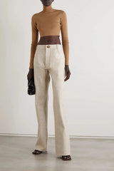 Person wearing a brown top, beige pants, and black gloves against a white background