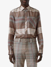 A model wearing a long-sleeve button-up shirt and matching trousers in a brown, beige, and red plaid pattern, photographed against a light gray studio background.