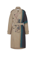 A beige trench coat with a vertical color-blocked panel in dark navy and teal, featuring a floral print on the front and a matching belt, shown against a light gray background.