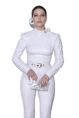 Person wearing a white outfit with a high collar and pants, holding a clutch.