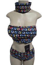 Mannequin wearing a colorful patterned bikini set with a matching neck scarf against a white door background.