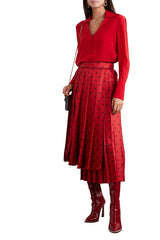 Person wearing a red outfit with a patterned skirt and high-heeled boots against a white wall.