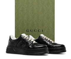 Black Gucci low-top sneakers with white laces, displayed in front of a green Gucci box on a white background.