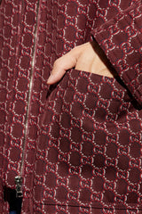 Close-up of a dark brown quilted jacket featuring an allover red and beige Gucci GG monogram pattern, with a hand tucked into a pocket.