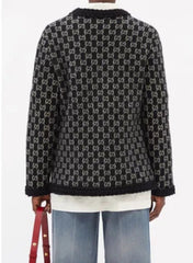 A black knit cardigan featuring an all-over white interlocking monogram pattern, shown from the back on a model wearing blue jeans and a white shirt.