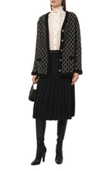 A model wears a black and white GG monogram tweed cardigan over a white lace mock-neck top, paired with a black pleated skirt, black knee-high leather boots, and a small black handbag against a plain white background.