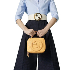 Person holding a yellow handbag with a visible brand logo against a light green background