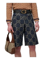 Person wearing Gucci patterned shorts and holding a matching handbag on a white background