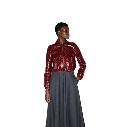 A model wearing a shiny dark red long-sleeve top and a dark gray skirt, standing against a plain light gray background.