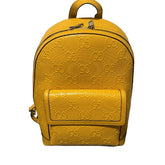 Yellow backpack with a prominent brand logo on a black surface against a beige wall.