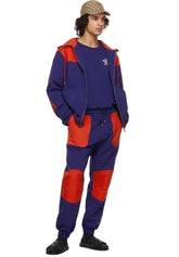 Person wearing a blue and red outfit with a cap on a plain background