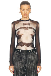 Model wearing a sheer top with lace details and high-waisted pants on a white background