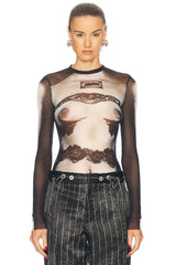 Model wearing a sheer top with lace details and high-waisted pants on a white background