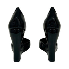 A pair of black patent leather high-heeled pumps shown from the back, featuring a pointed toe and a chunky block heel, set against a plain white background.