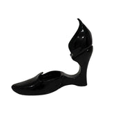 A single black patent leather wedge shoe with a unique sculptural heel and pointed toe, shown against a plain white background.