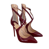 A pair of pointed-toe high-heel pumps in glossy deep burgundy patent leather, featuring crisscross ankle straps and a stiletto heel, displayed on a brown shoebox against a light off-white background.