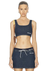 Woman wearing a dark blue denim sports bra and skirt with 'miu miu' branding on a white background.