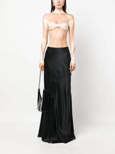 Woman wearing a strapless beige top and black satin skirt holding a handbag on a white background