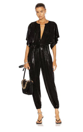 Woman wearing a black vinyl jumpsuit holding a handbag on a white background