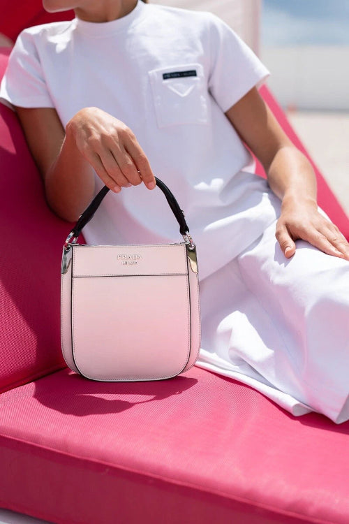Person holding a pink handbag on a pink surface with a blurred background