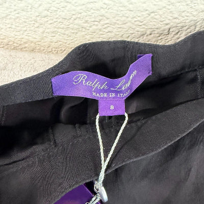 A close-up of a black garment with a purple brand tag reading 'Sartoria' on a textured light beige background.
