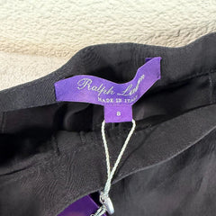 A close-up of a black garment with a purple brand tag reading 'Sartoria' on a textured light beige background.