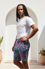 Man wearing a white t-shirt and colorful shorts standing in front of a white archway with cacti.