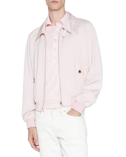 A model wearing a light pink zip-up jacket over a matching pink polo shirt and white trousers, photographed against a plain light gray studio background.