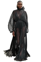 Model wearing a black, flowing dress on a fashion runway with an audience.