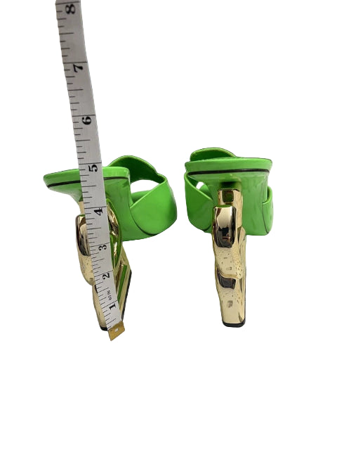 Green shoes with gold buckles on a perforated surface, measured by a tape measure.