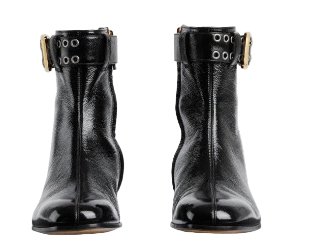 Pair of black leather ankle boots with gold buckles on a light gray background
