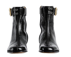 Pair of black leather ankle boots with gold buckles on a light gray background