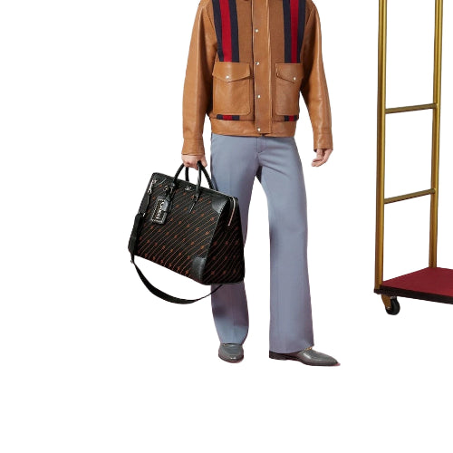 Person holding a black leather bag wearing a brown jacket with red and blue stripes, light blue pants, and gray shoes on a pink floor.