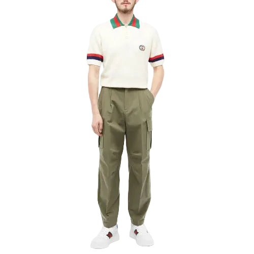 Person wearing a cream polo shirt with red and green accents and olive green cargo pants on a white background