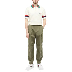 Person wearing a cream polo shirt with red and green accents and olive green cargo pants on a white background