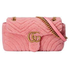 Pink quilted handbag with gold chain strap and logo on a light gray background